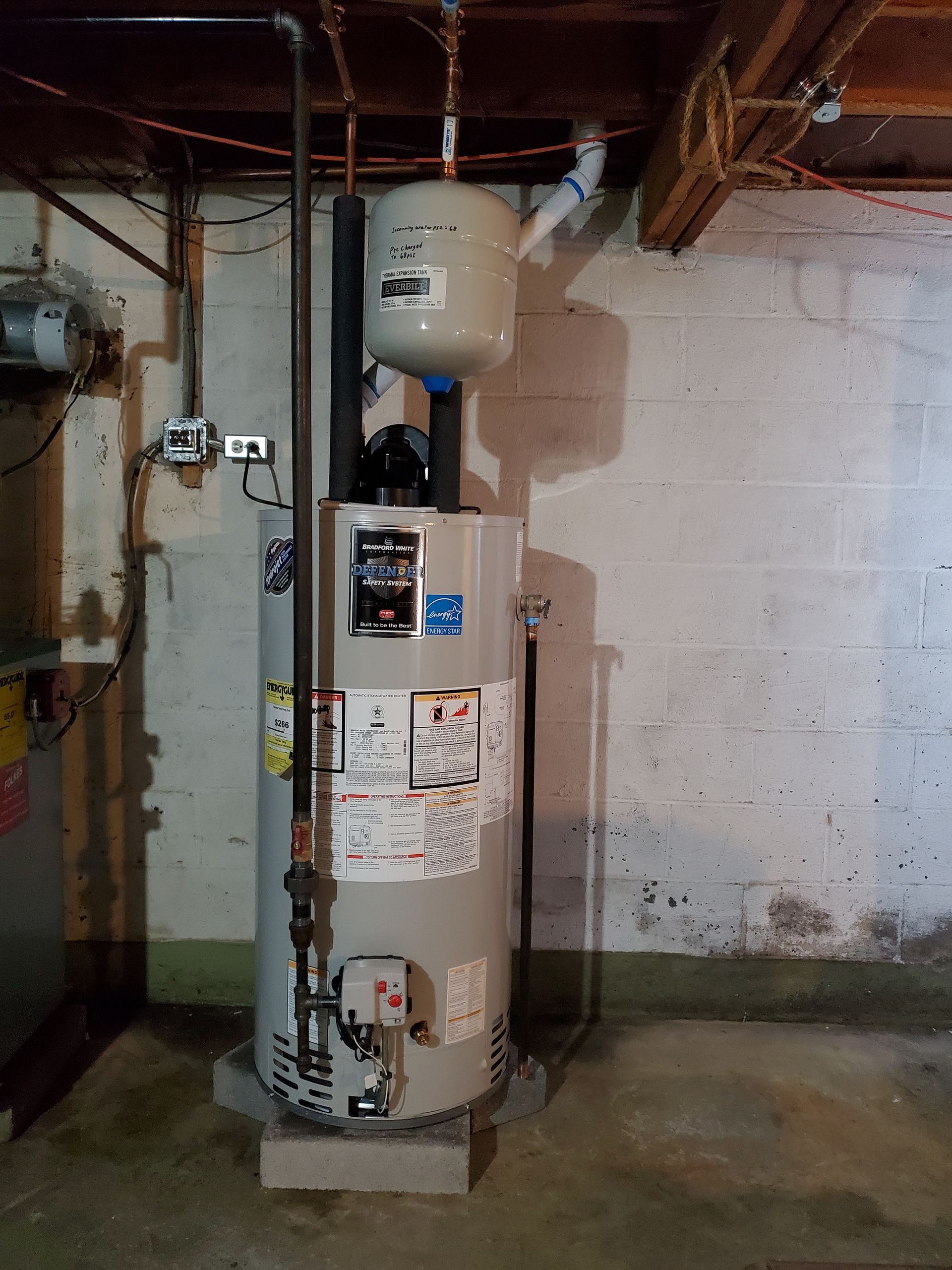 A water heater is sitting in a basement next to a wall.
