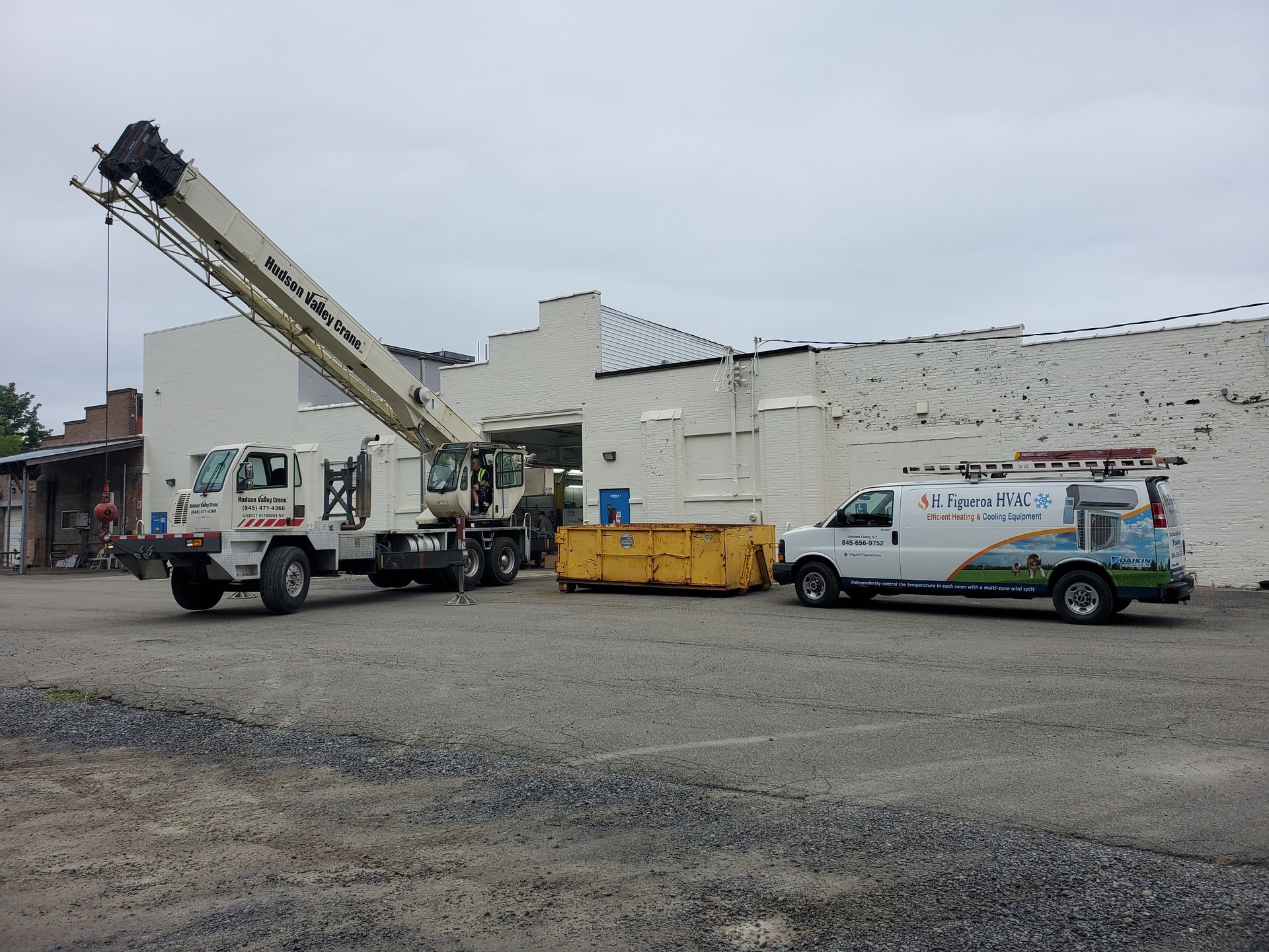 A crane and a van are parked in a parking lot in front of a building.