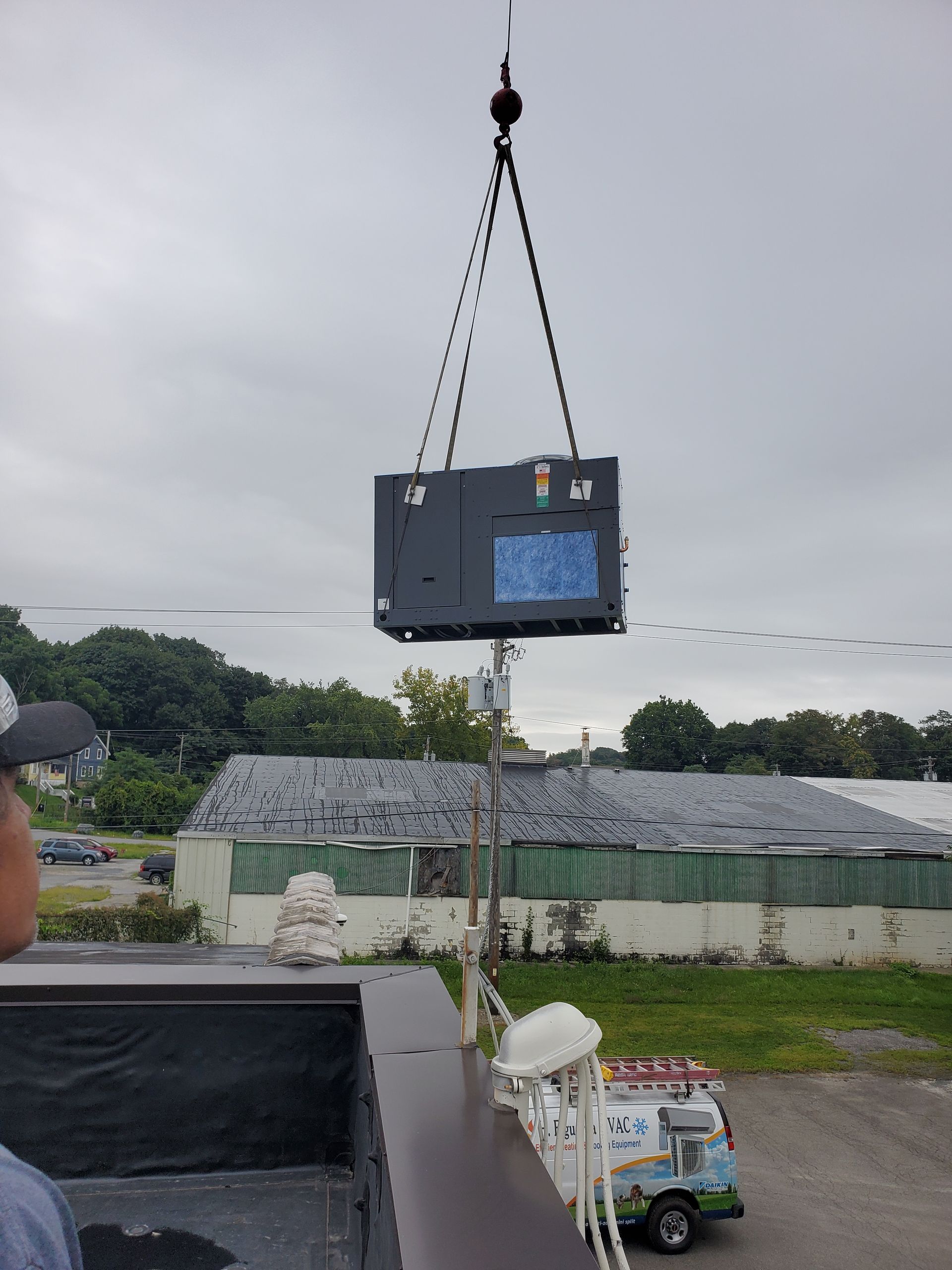 A man is standing in a truck looking at a crane lifting a box.