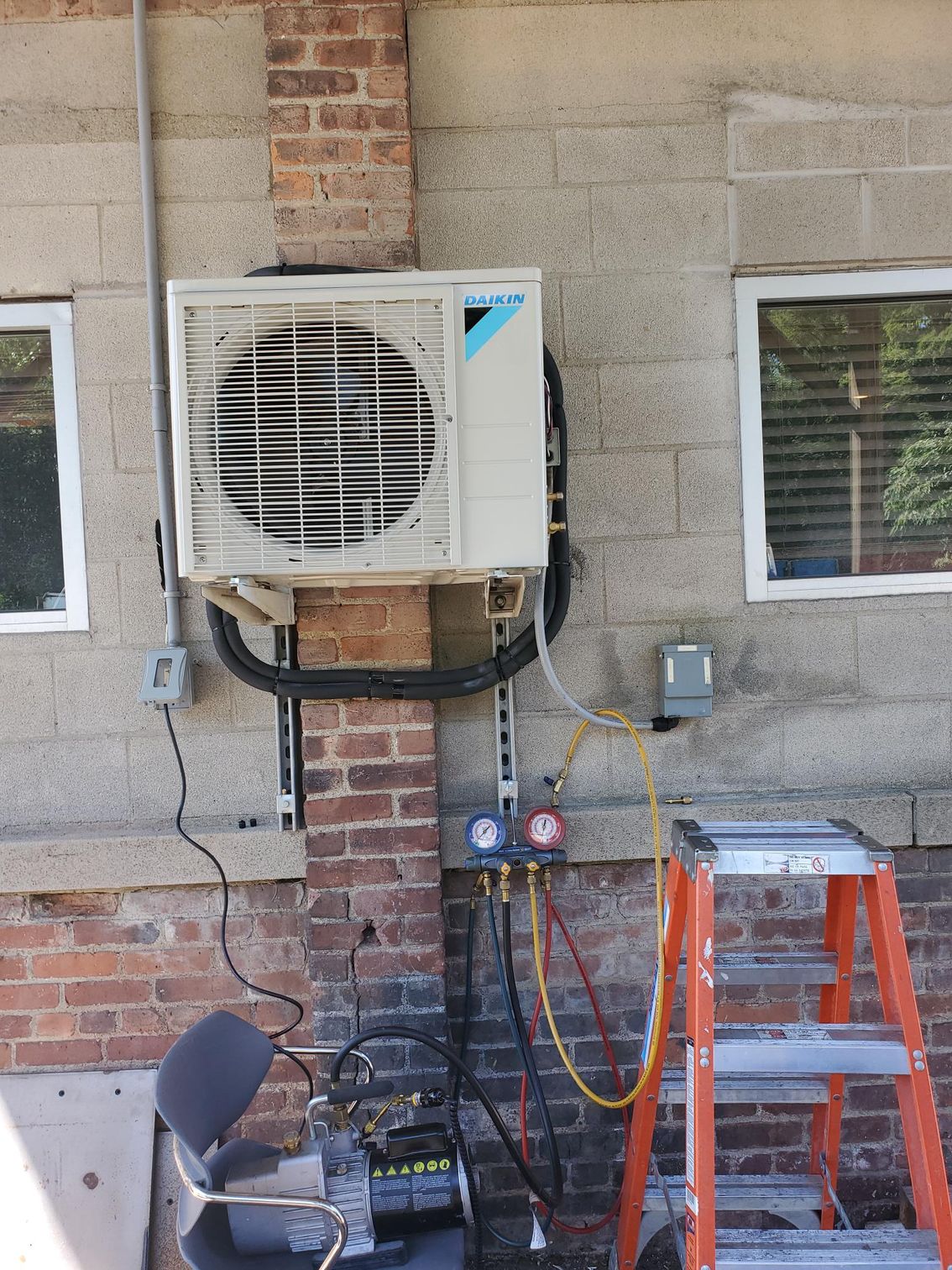 An air conditioner is mounted on a brick wall next to a ladder