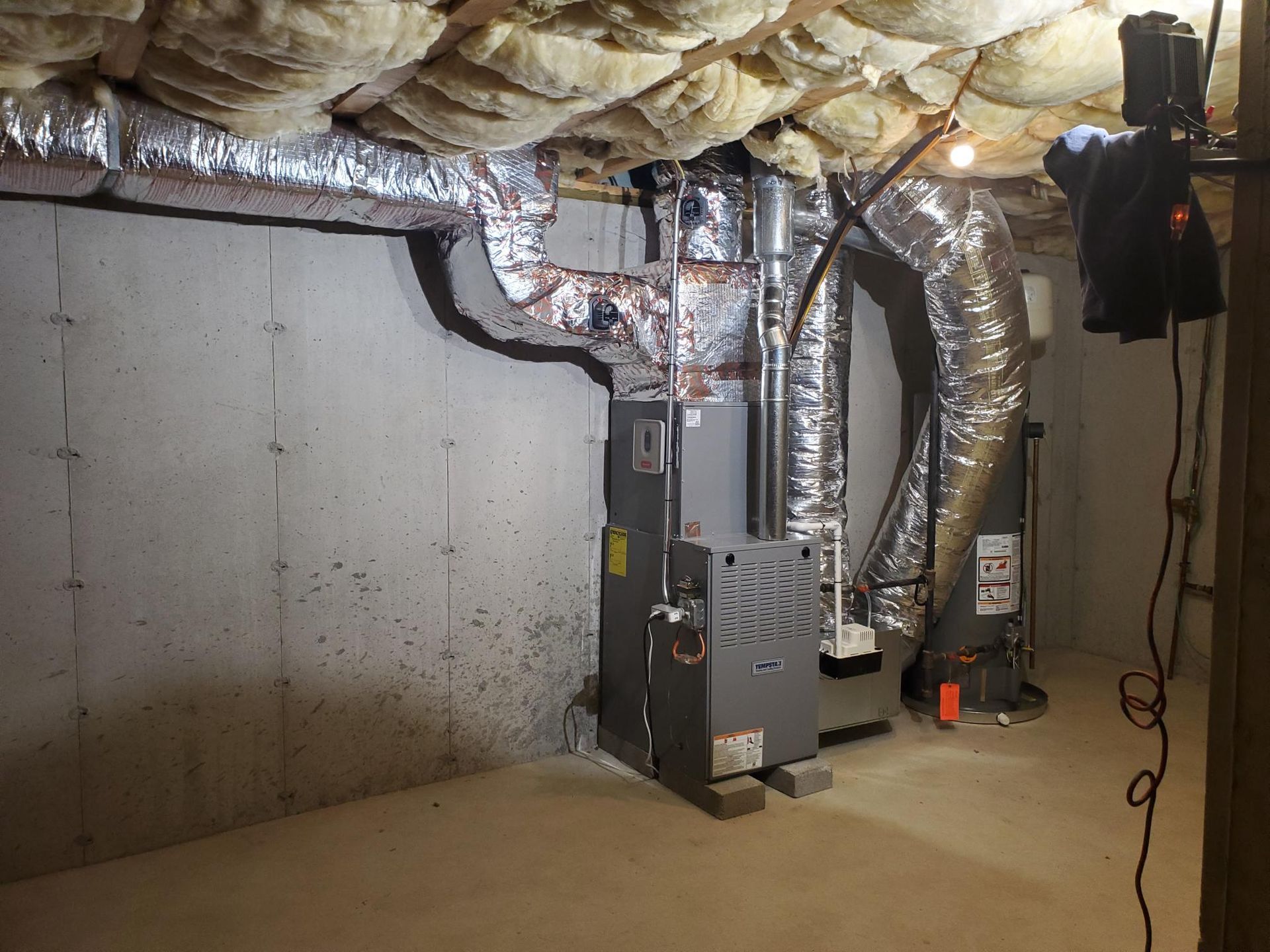 A basement with a furnace and ducts hanging from the ceiling.