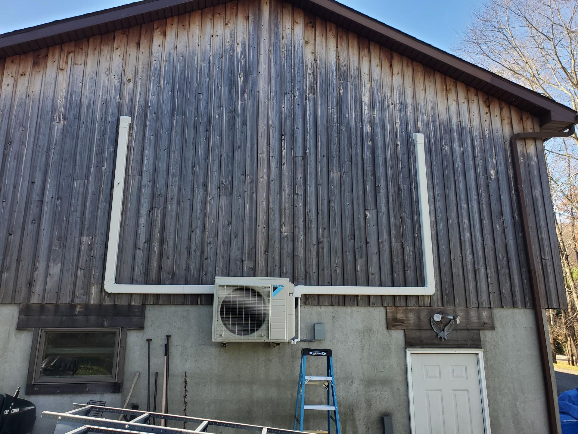 An air conditioner is mounted on the side of a wooden building.