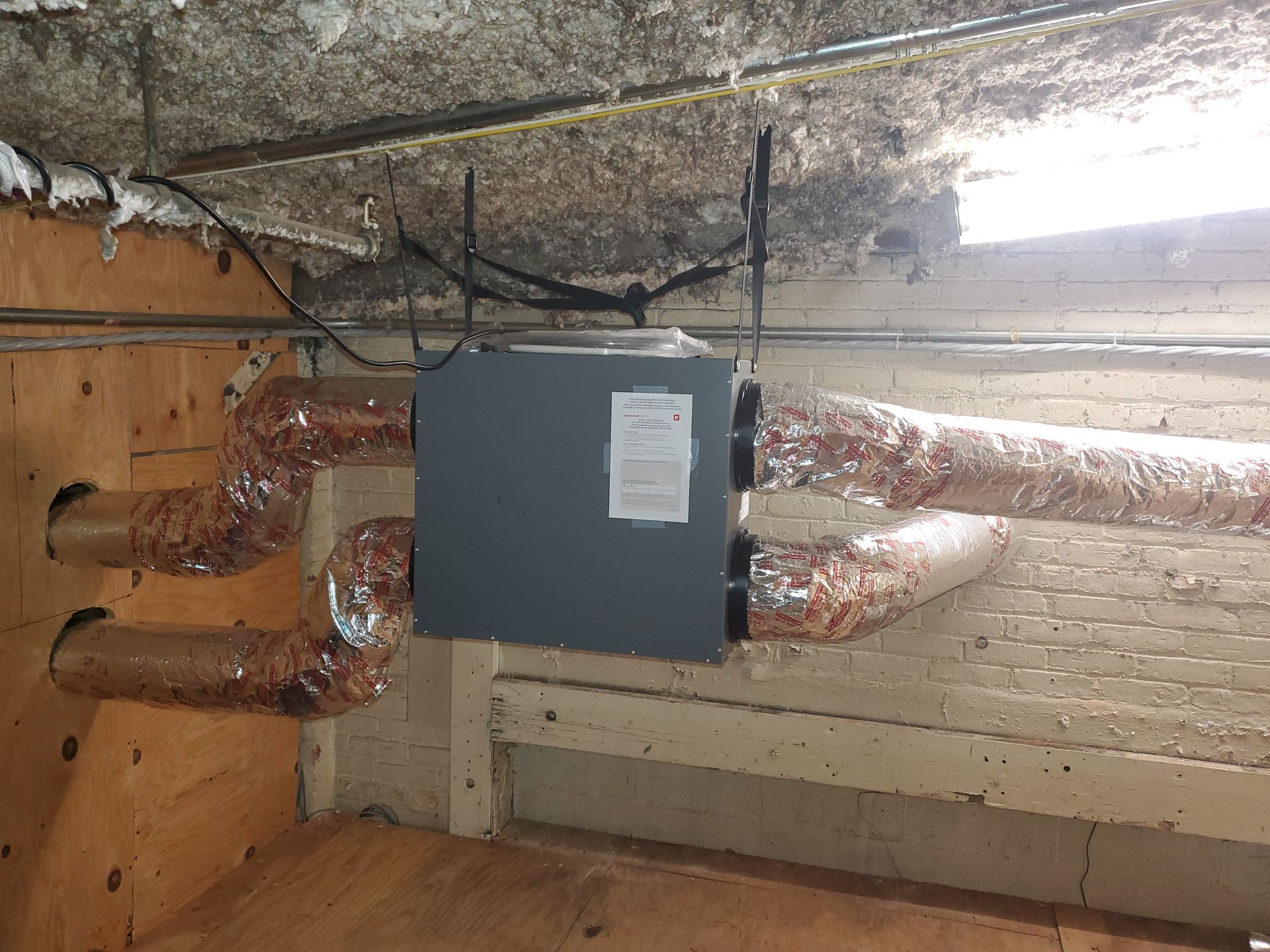 A box is hanging from the ceiling of a room with pipes coming out of it.