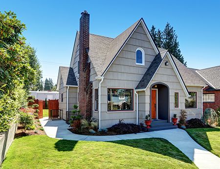 A gray house with a gabled roof, orange front door, and brick chimney, sitting on a green lawn.