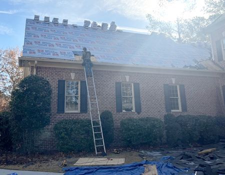 A man on a ladder is working on the roof of a brick house.