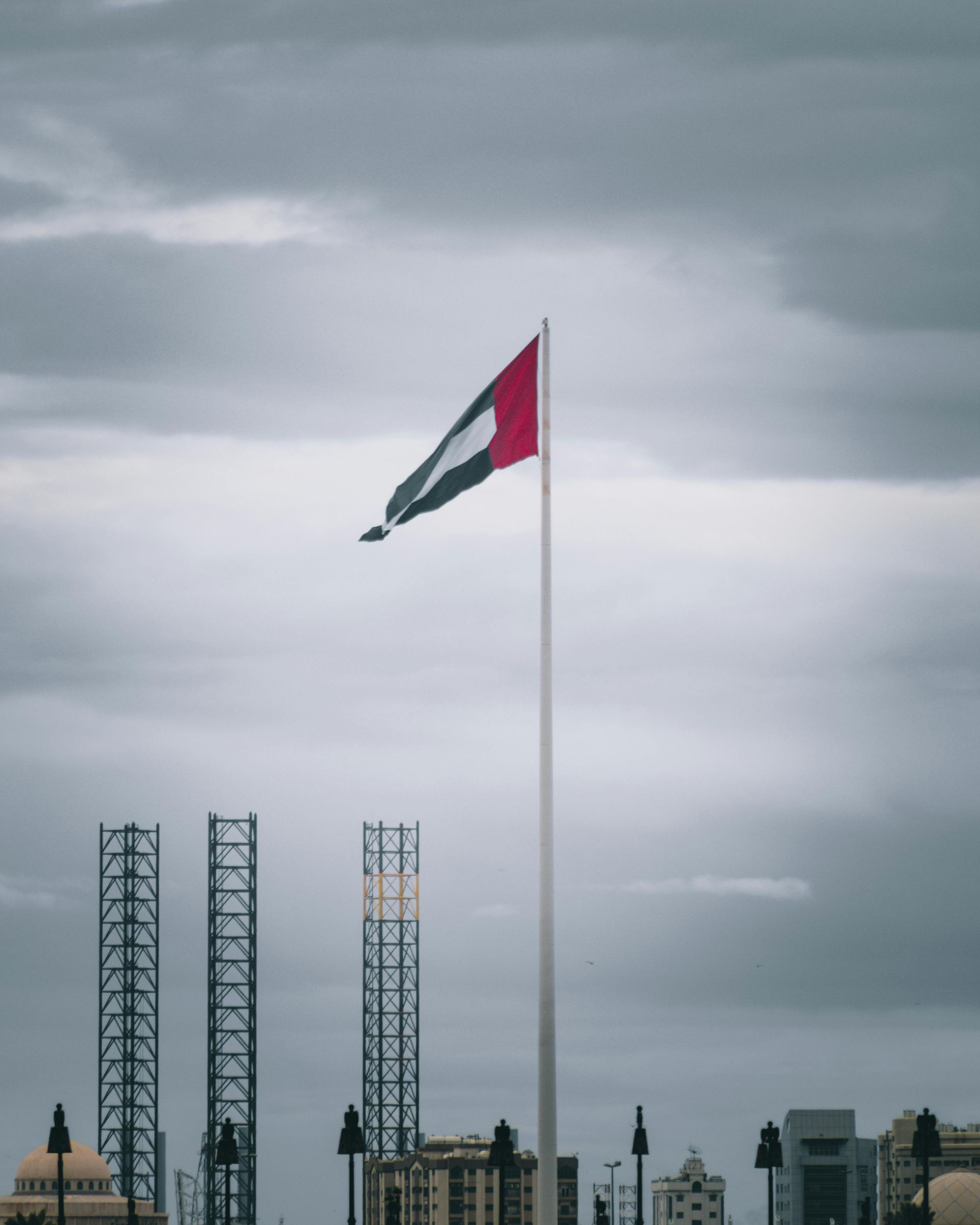 United Arab Emirates flag waving against a cloudy sky with architectural structures in the background.