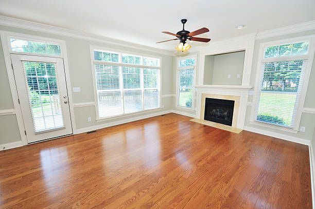 An empty living room with hardwood floors , a fireplace and a ceiling fan.
