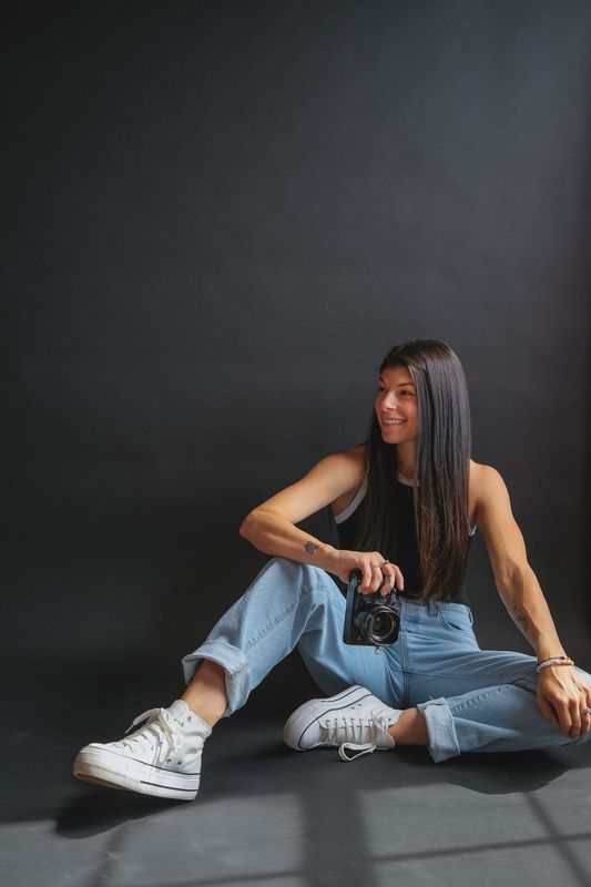 A woman is sitting on the floor holding a camera.