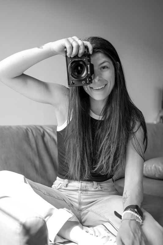 A woman is sitting on a couch taking a selfie with a camera.