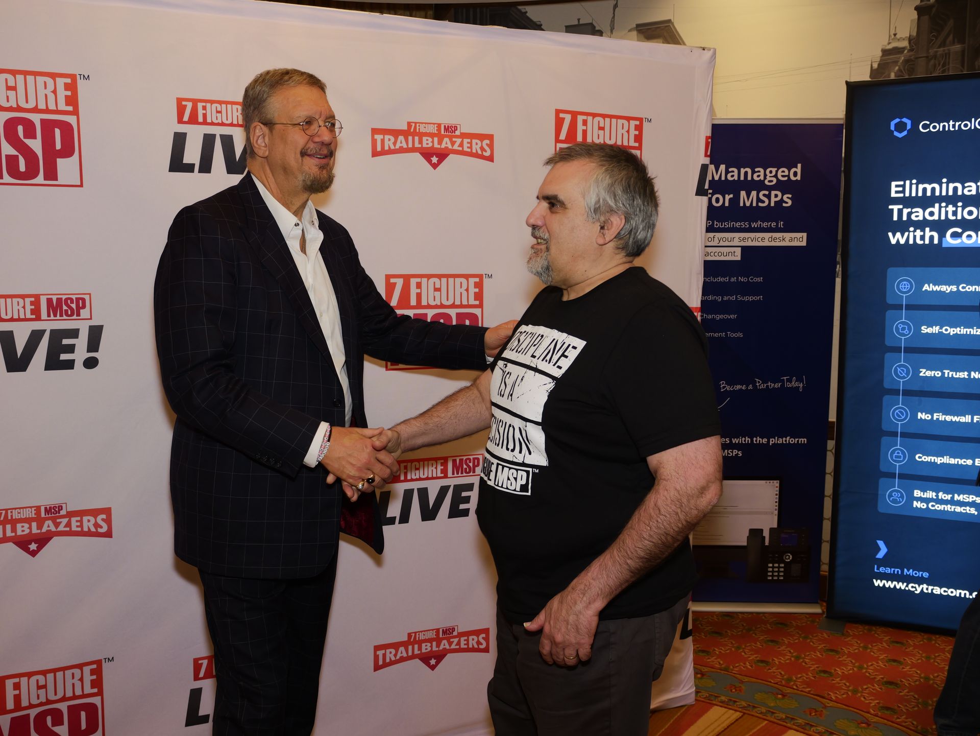 Two men shaking hands in front of a wall that says figure sp