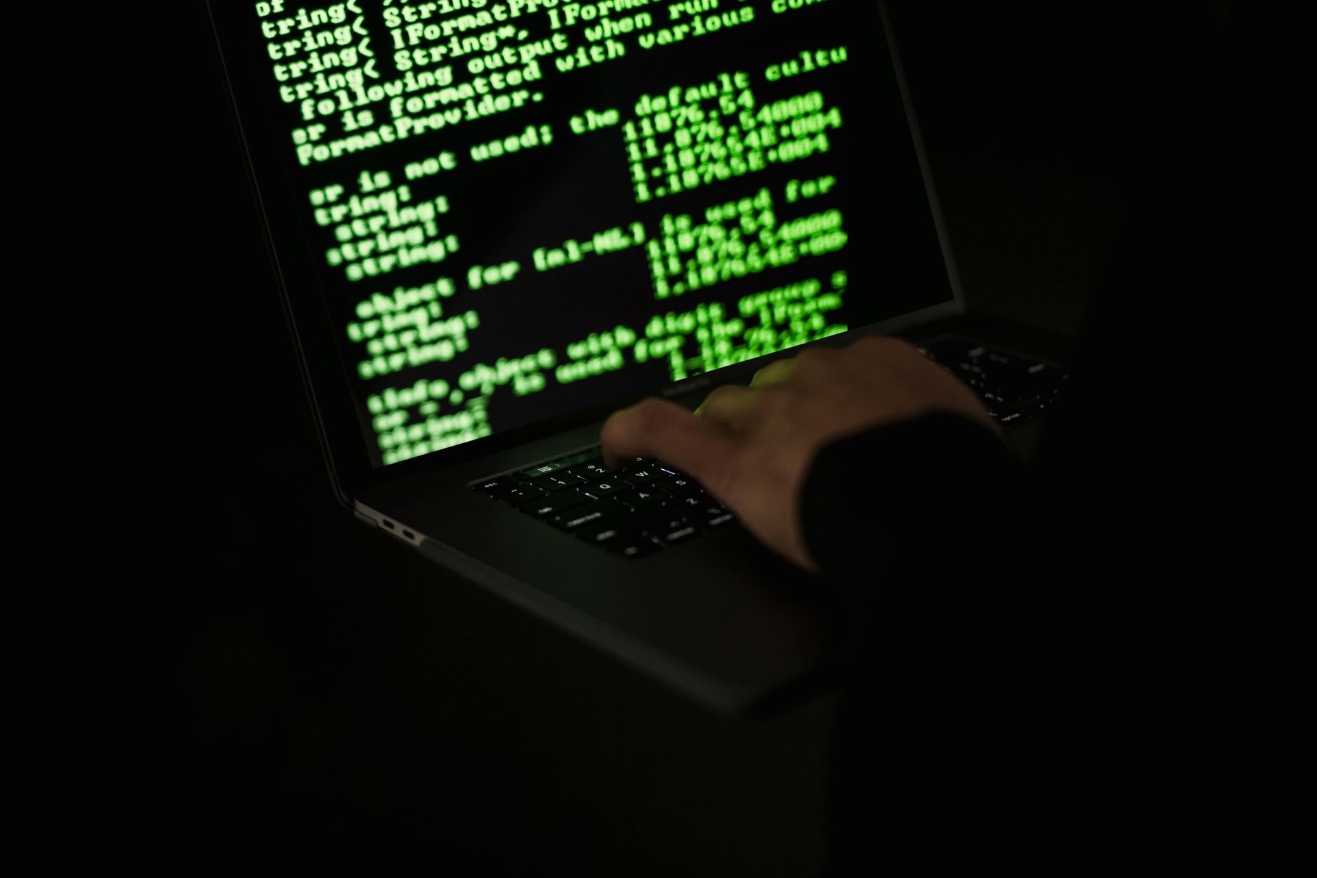 A person is typing on a laptop with green text on the screen