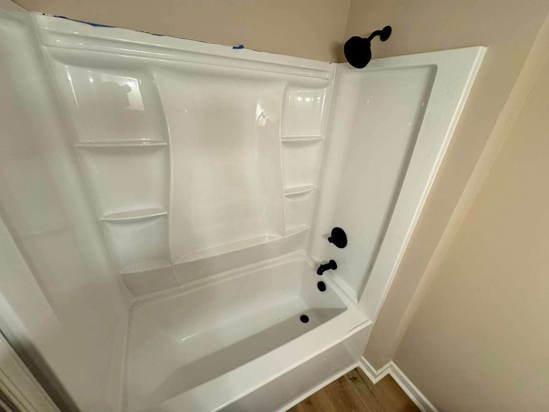 White corner bathtub with black fixtures, shower curtain and shelves, in a bathroom.