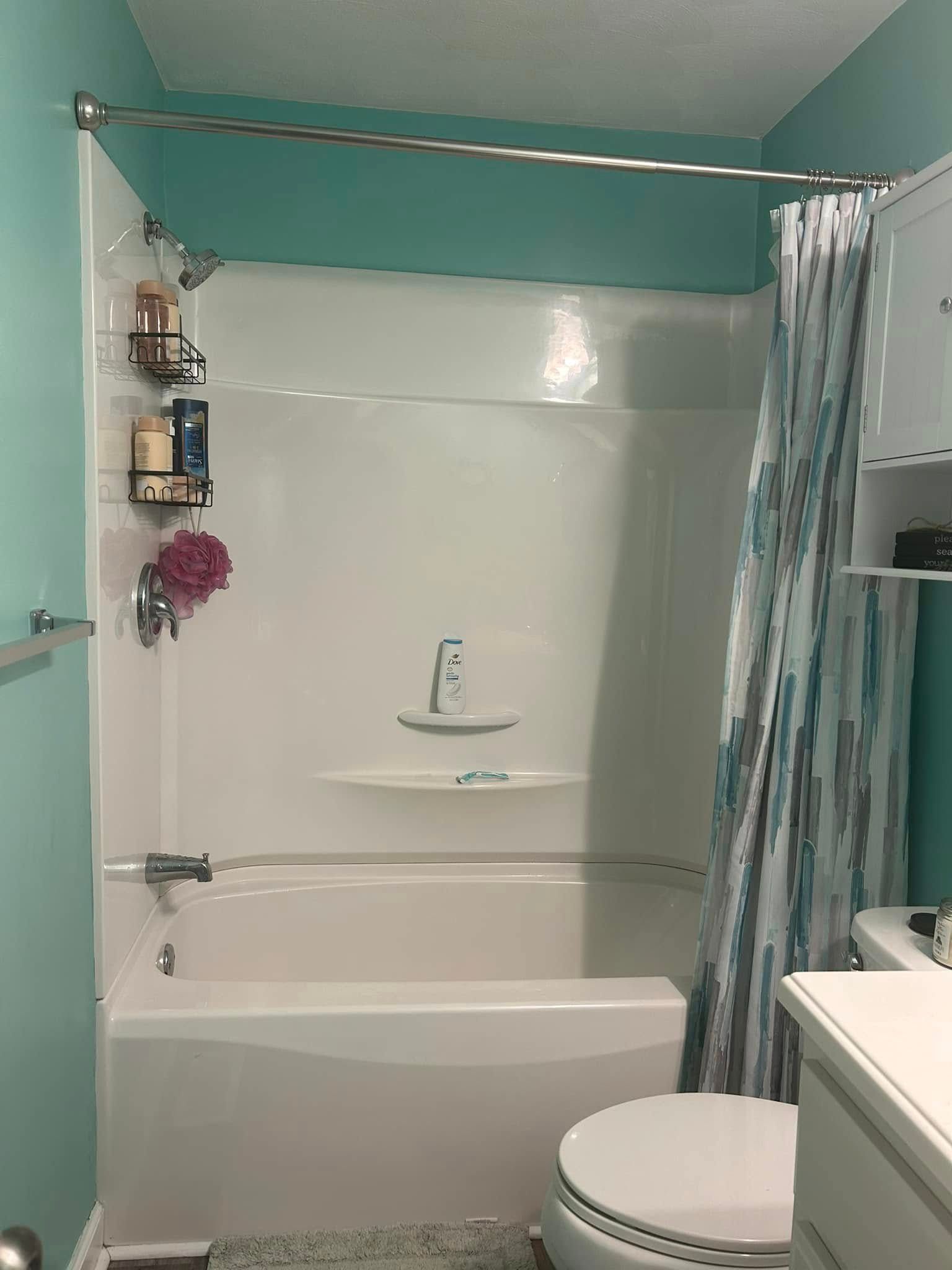 White bathroom with turquoise walls. White tub and shower combo with curtain, toilet, and shelving.