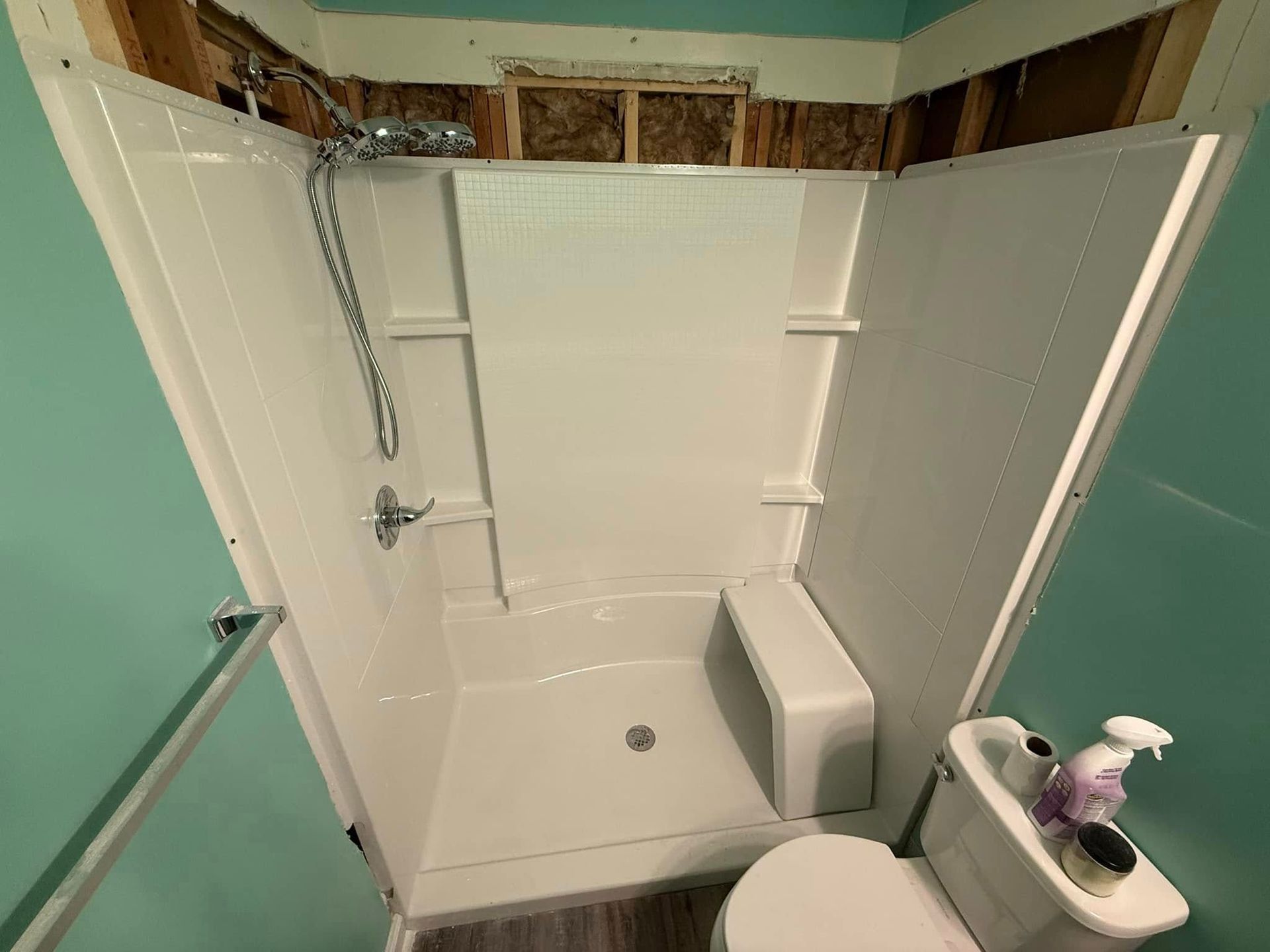White walk-in shower with bench and grab bar, surrounded by blue walls and exposed wooden framing.