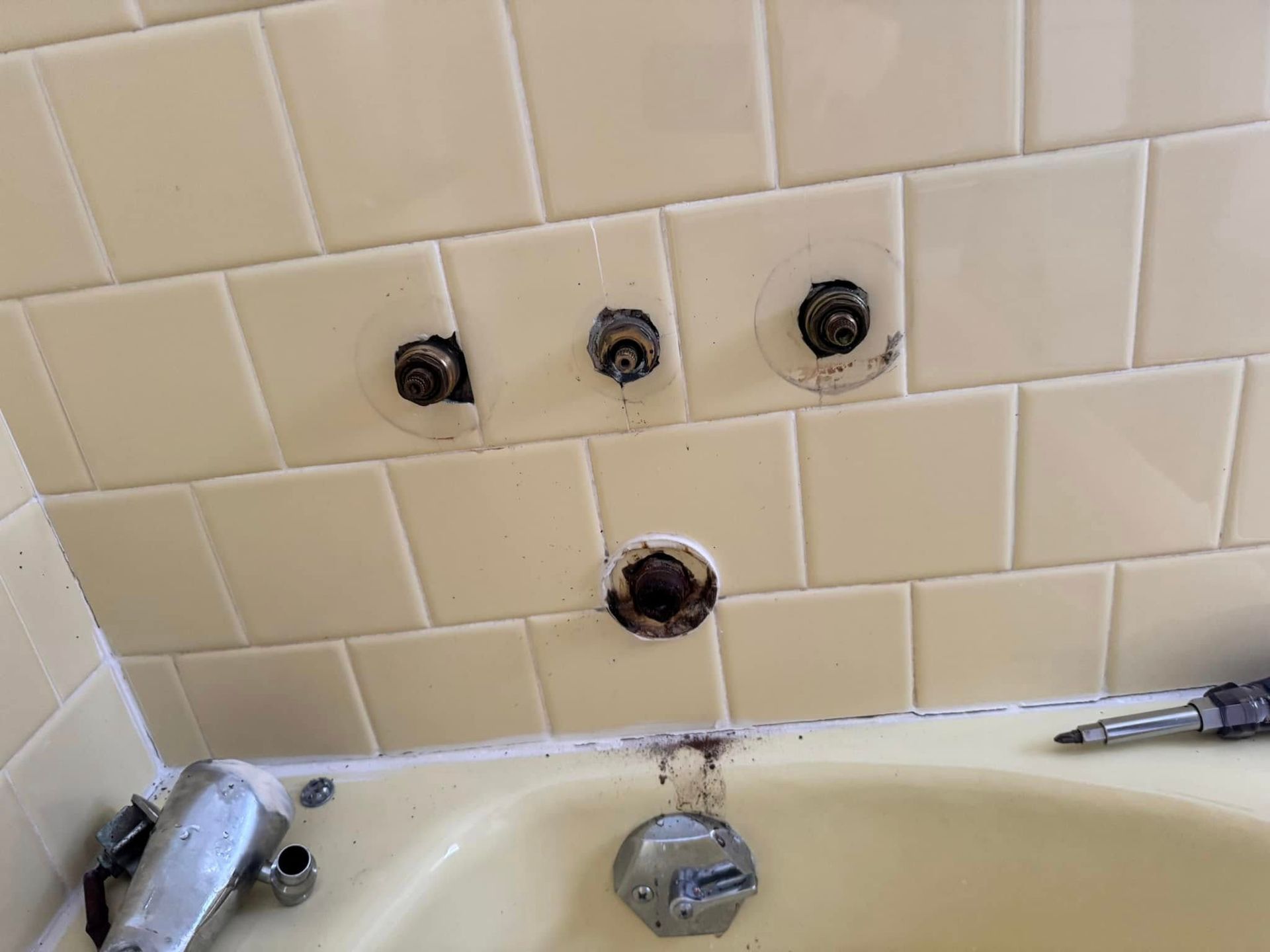 Bathtub plumbing fixtures exposed on tile wall. Rust and discoloration present.