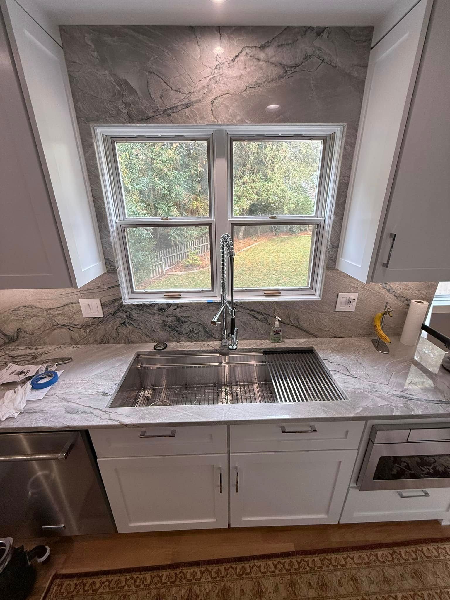 Kitchen with white cabinets, stainless steel sink, granite countertop, and a window overlooking trees.
