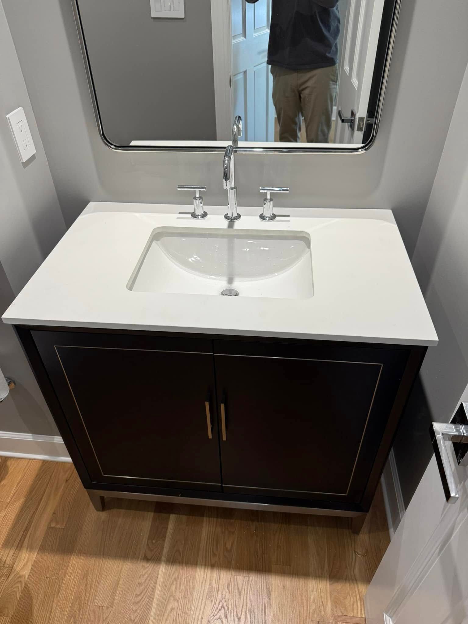 Dark bathroom vanity with white countertop and sink, chrome faucet, and rectangular mirror.