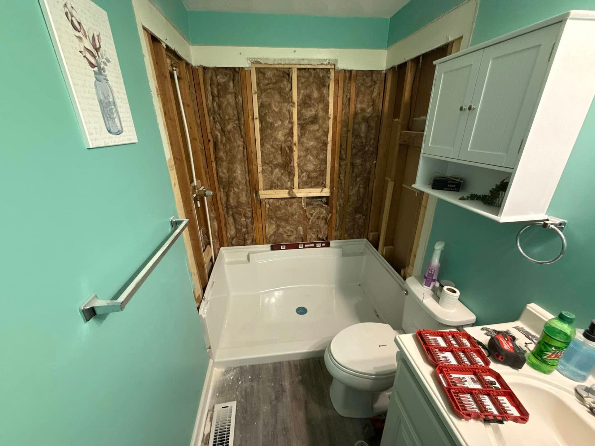 Bathroom renovation in progress; exposed studs, shower base installed, turquoise walls, and a mounted cabinet.