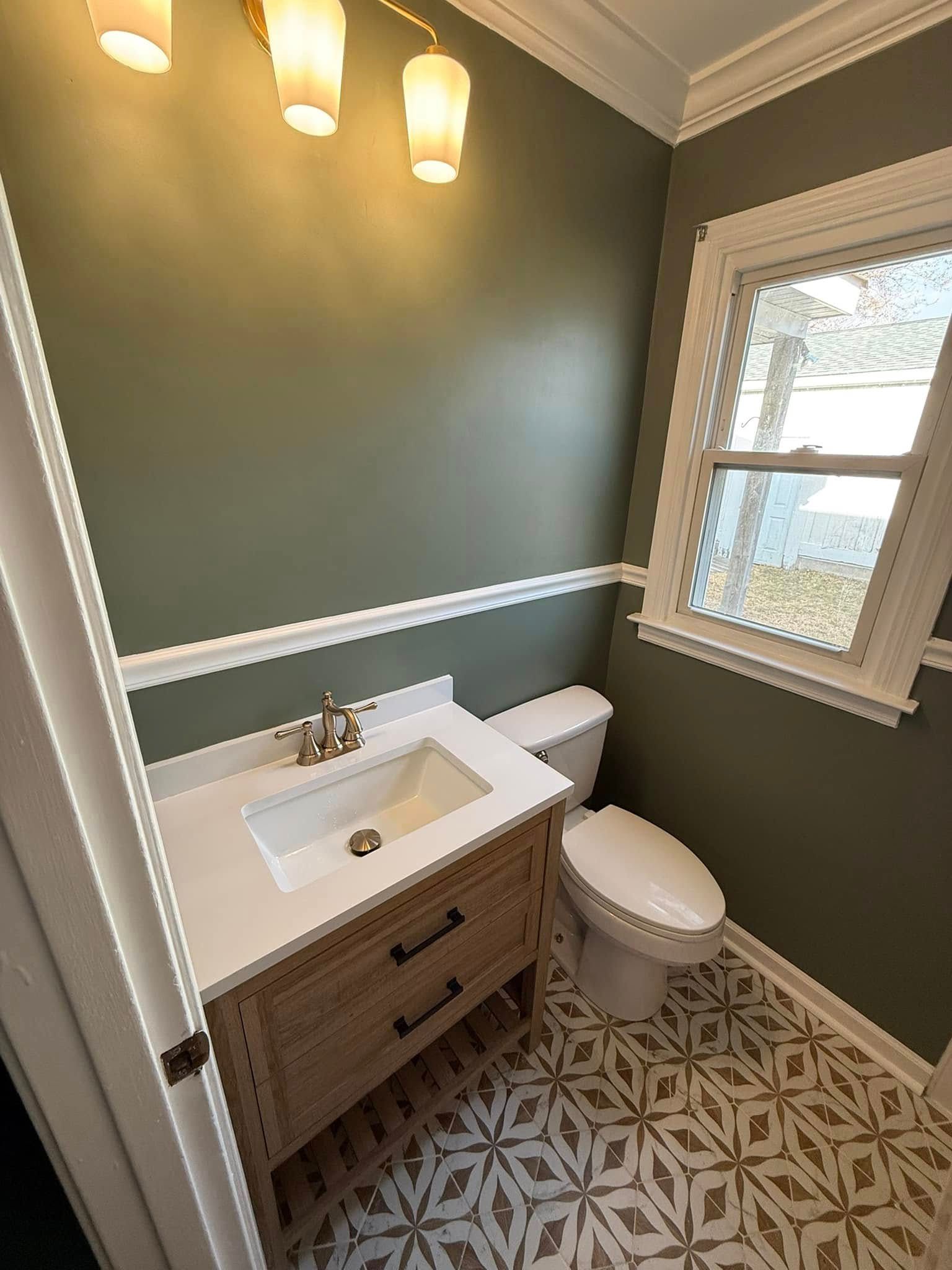 Bathroom with green walls, a white vanity, a toilet, and patterned tile flooring.