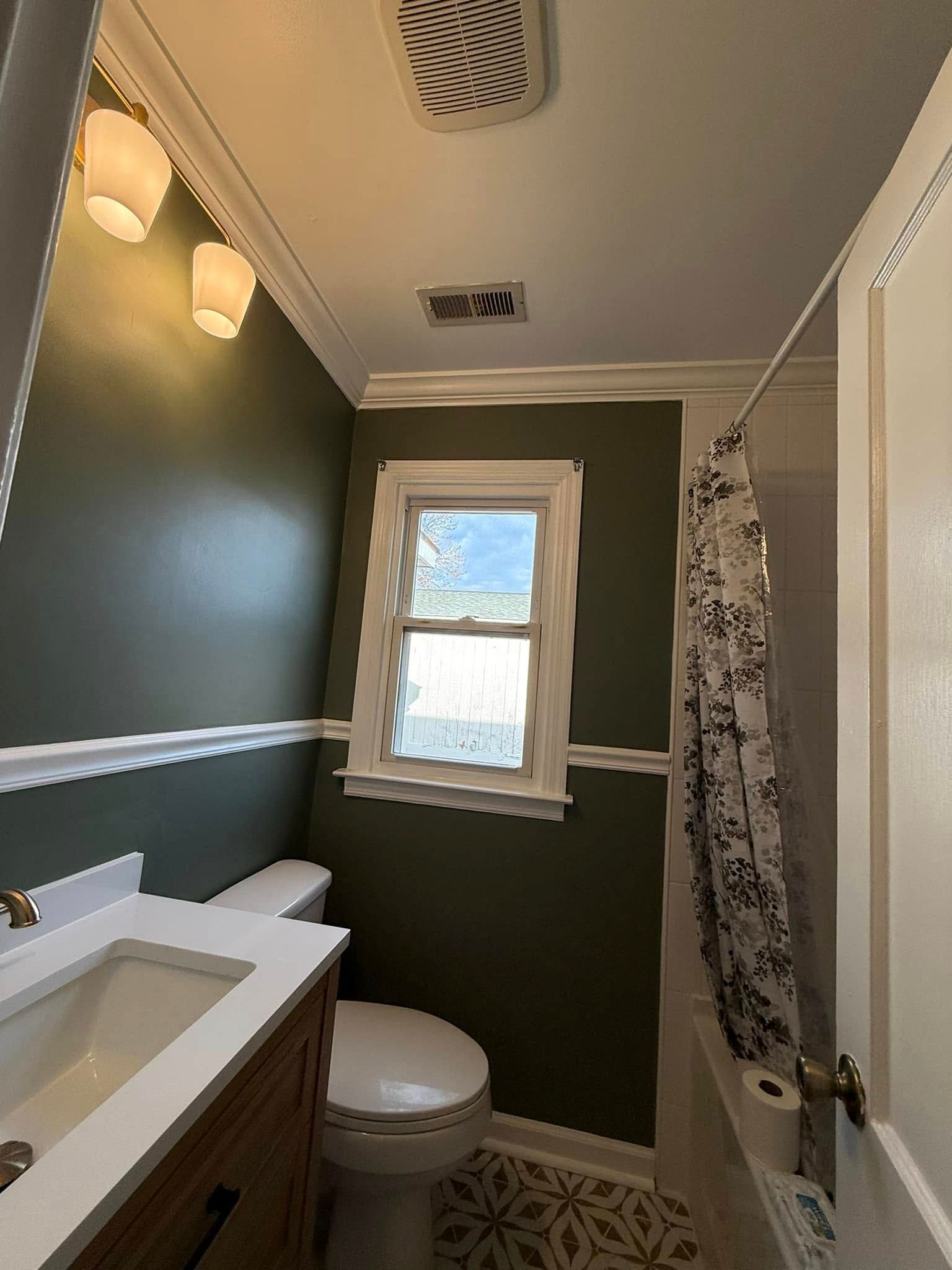 Bathroom with dark green walls, white trim, and a window above the toilet.