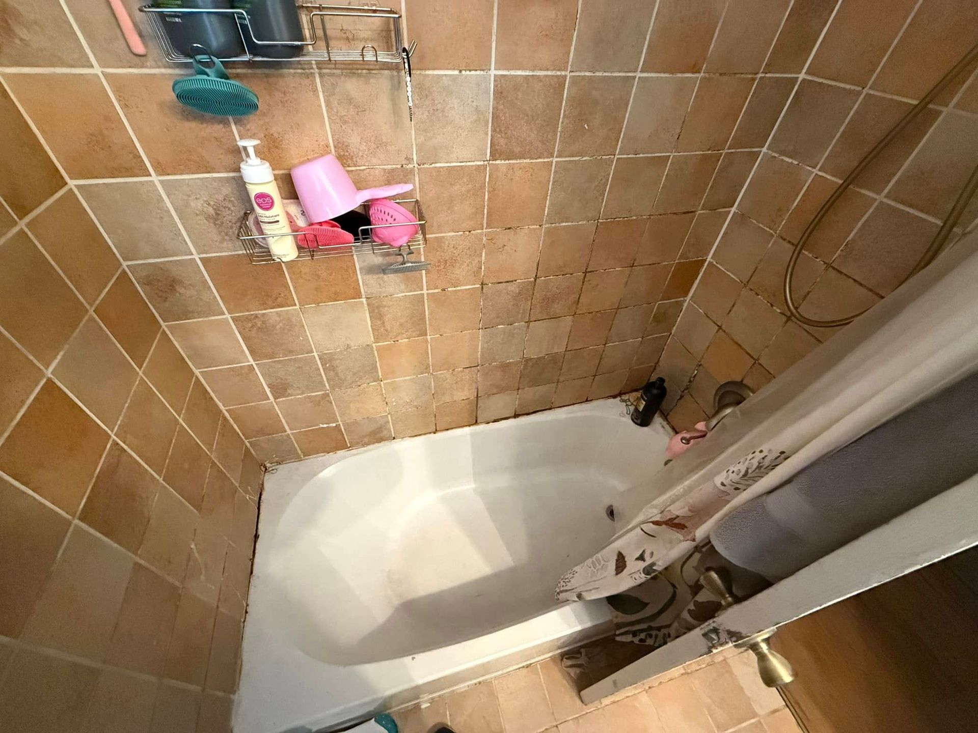 A shower stall with brown tile walls and a white bathtub. A shower curtain is partially drawn.