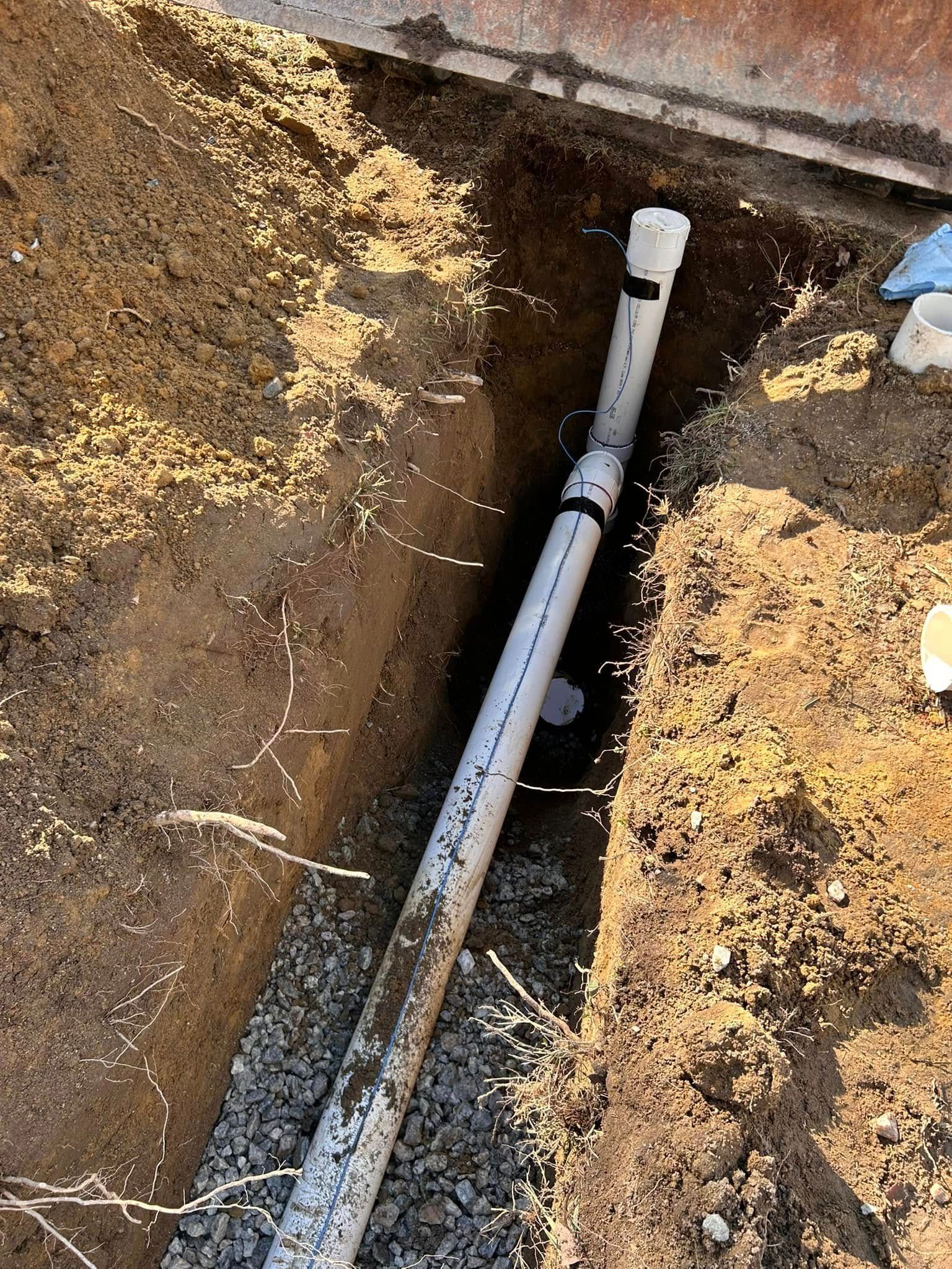 A PVC pipe in a trench next to a wall. The trench has gravel in the bottom.