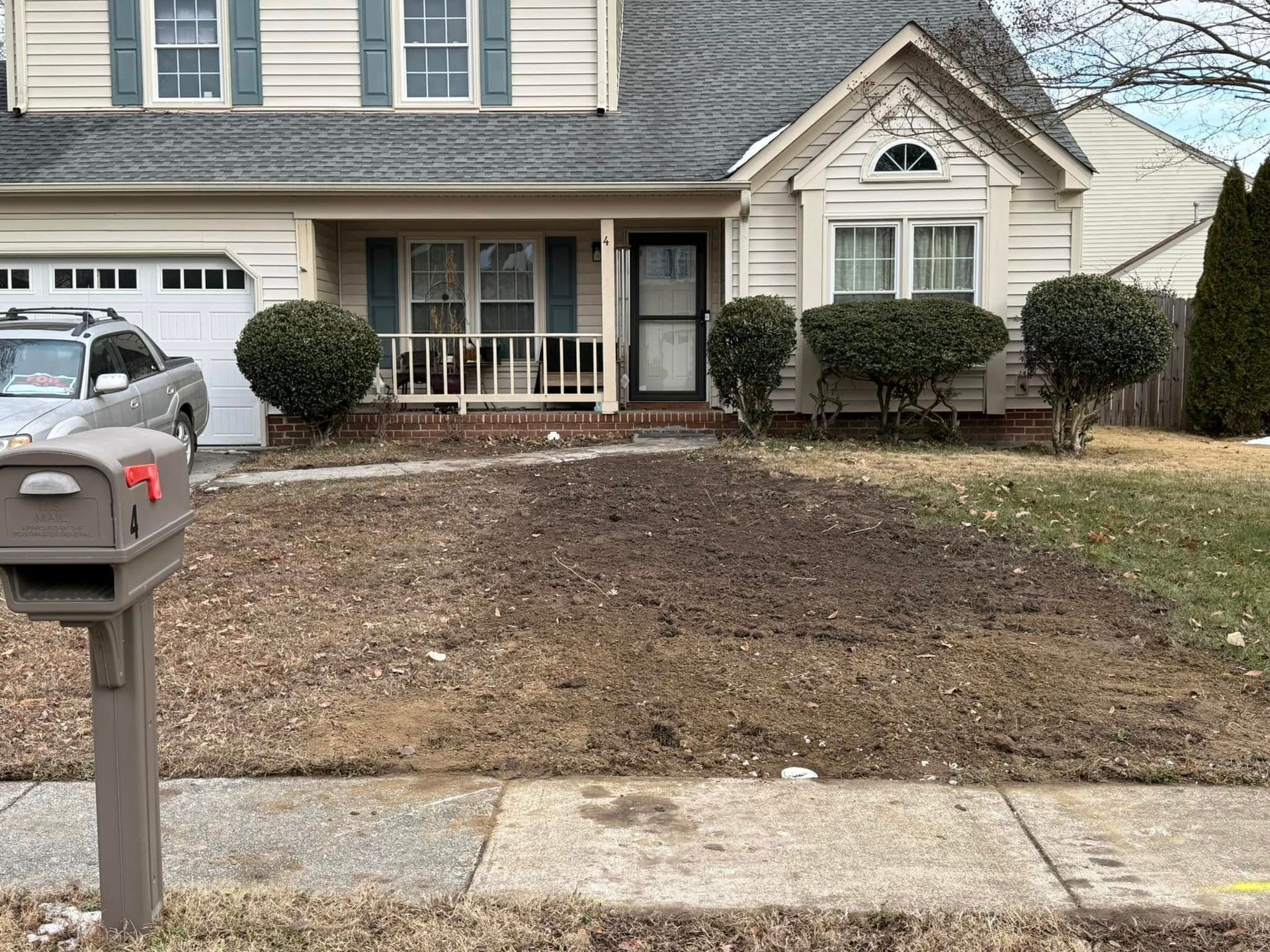 House with bare front yard; mailbox in foreground; car in the driveway.