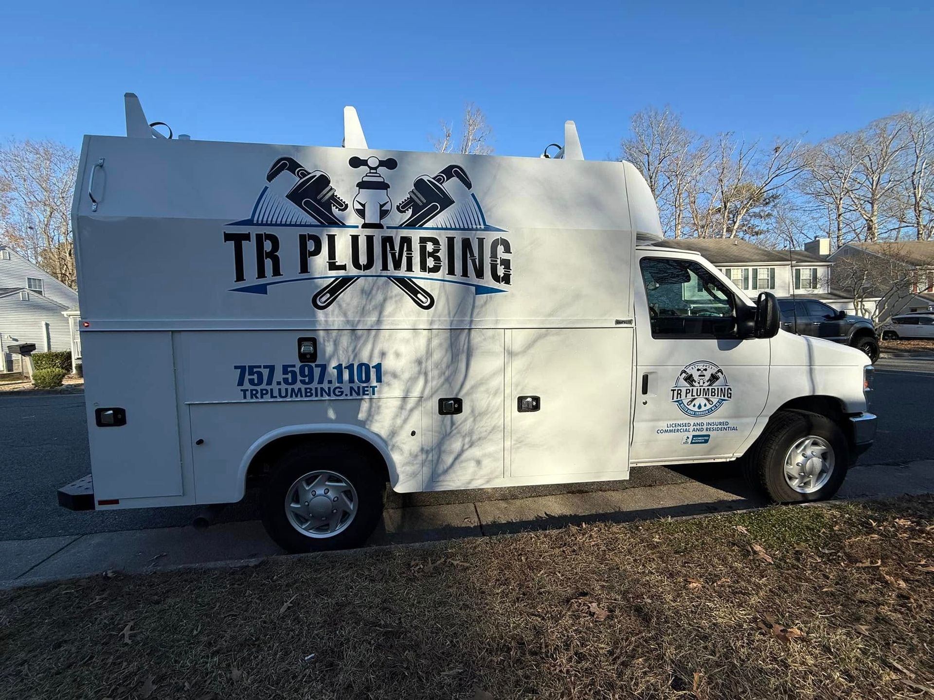 White TR Plumbing van with logo and contact info parked on street.