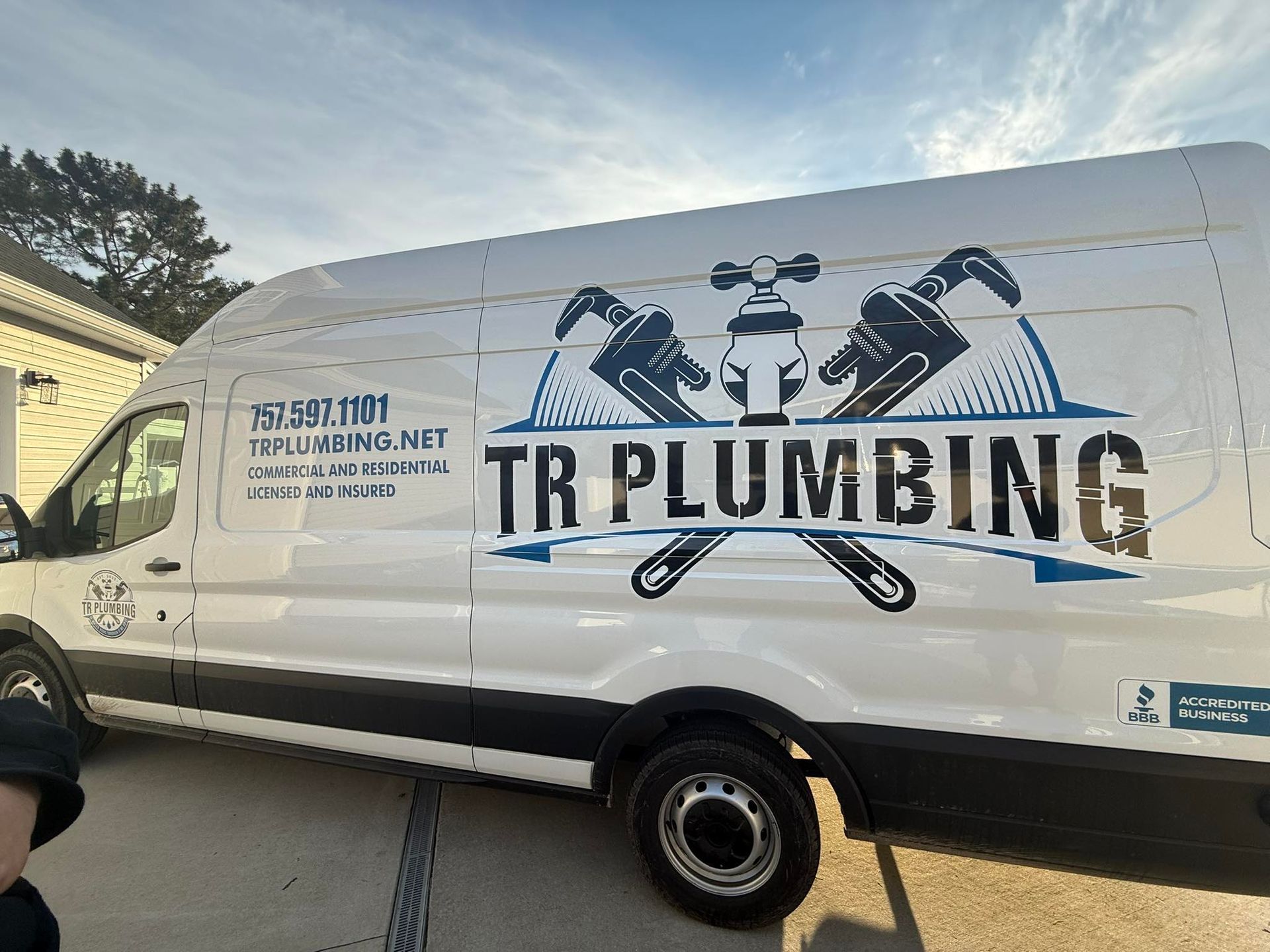 White TR Plumbing van with logo and contact info parked outside.