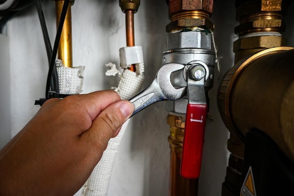 Hand using a wrench to tighten a valve on a copper pipe system, possibly for plumbing or heating.