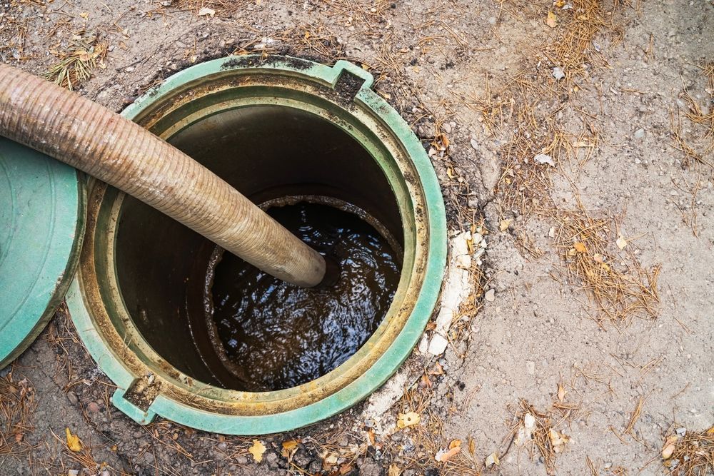A sewage tank being emptied by a large hose; tank is open with visible wastewater.