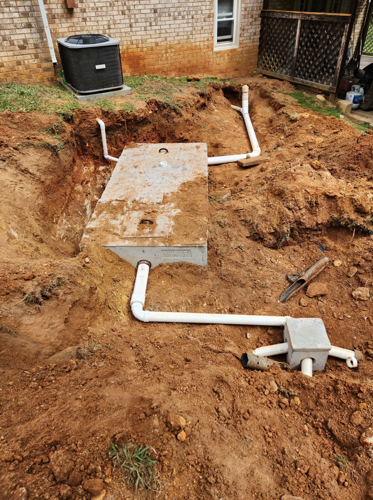 Construction site with a septic tank, pipes, and control box in a yard.