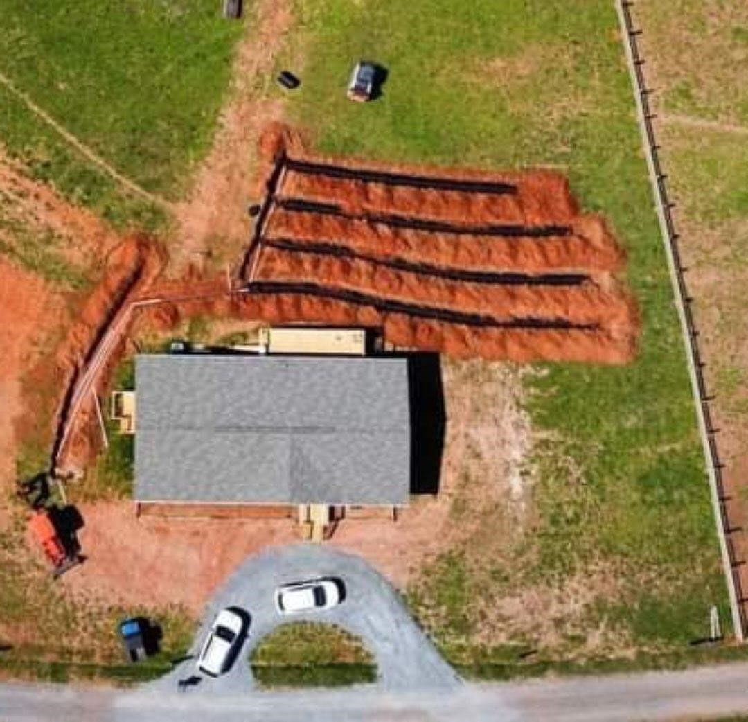 Aerial view of a house under construction with a gravel driveway and tiered soil beds nearby.