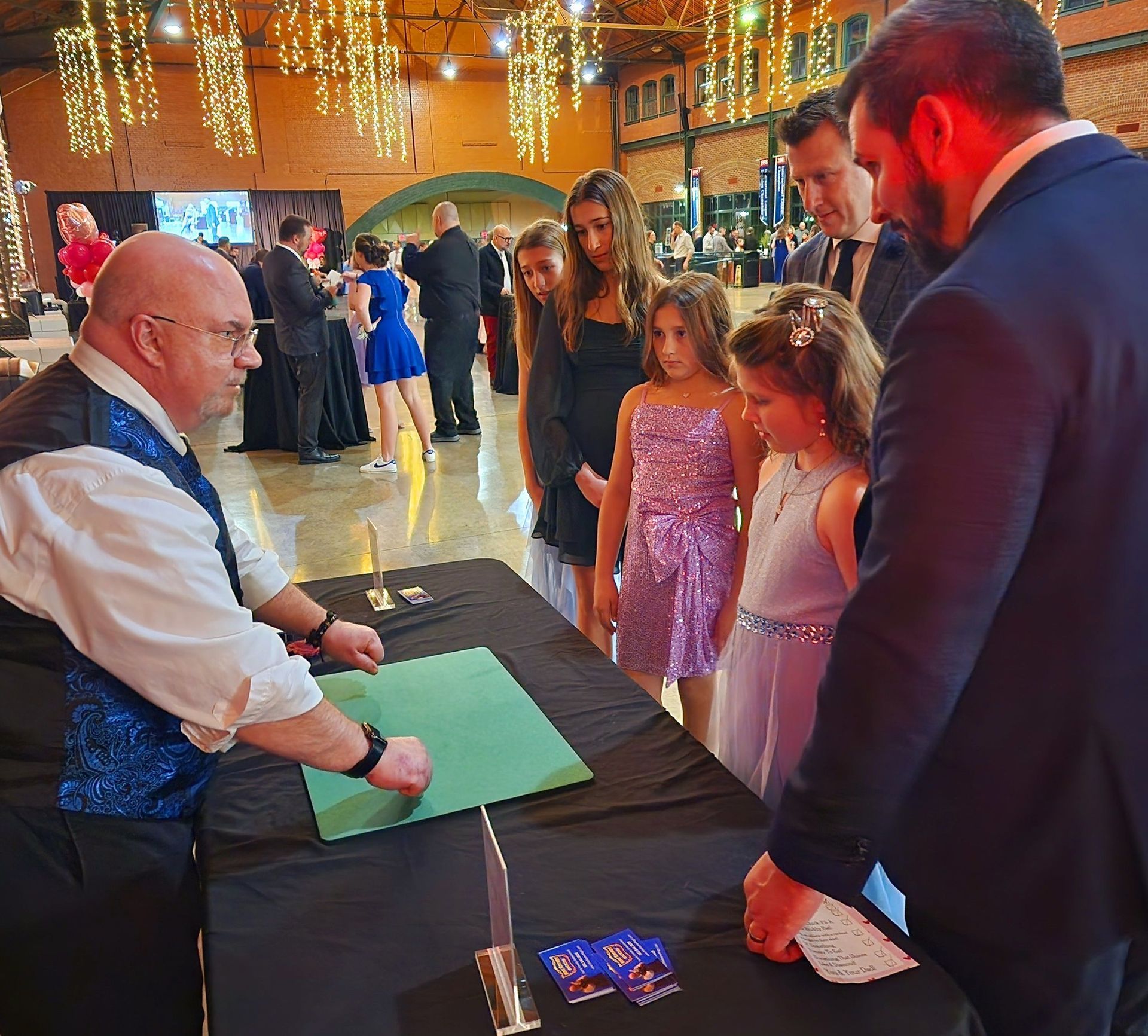 Magician performing for a group of people at a formal event, featuring a table with props.