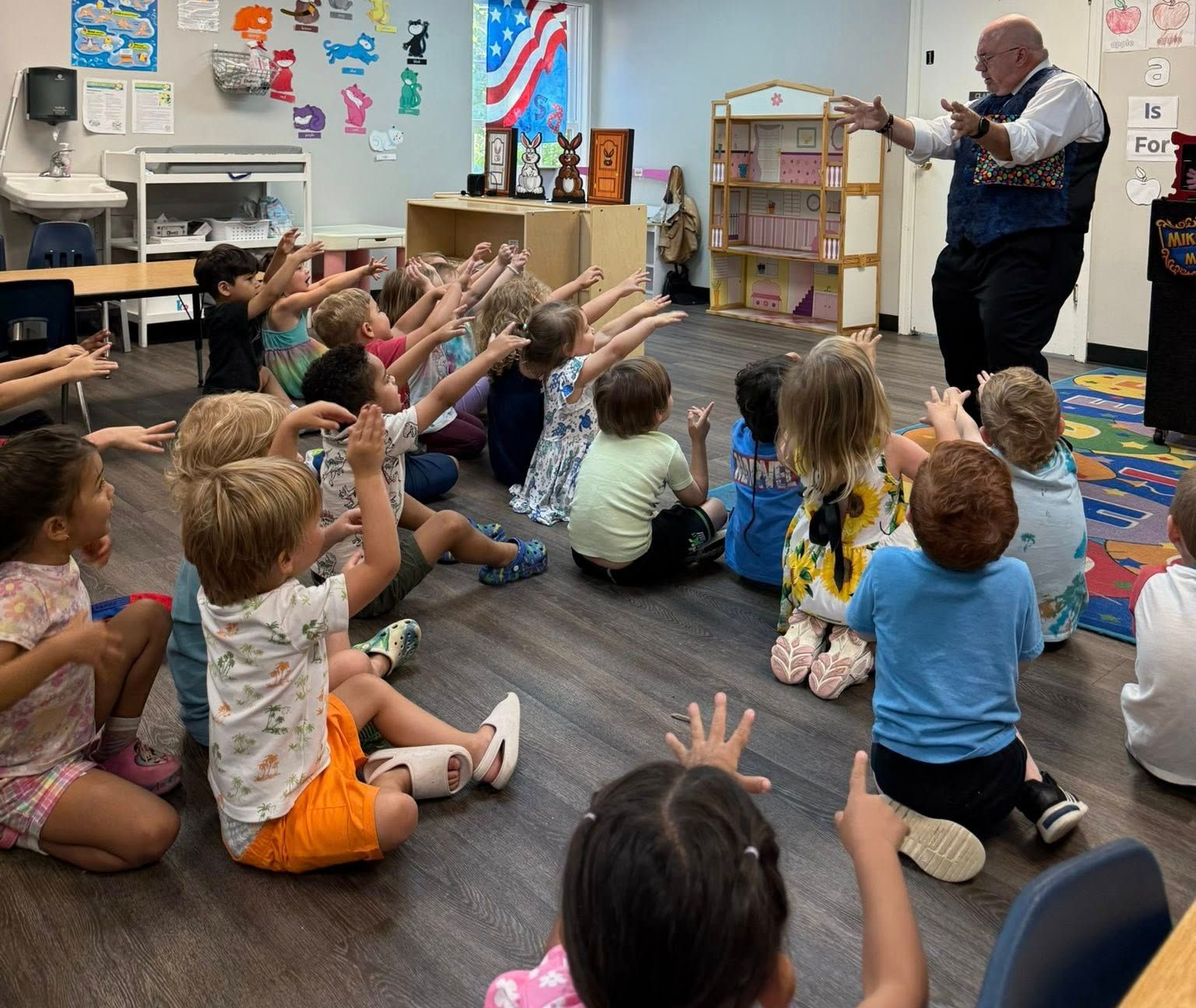 Children in a circle watch a man performing magic in a classroom.