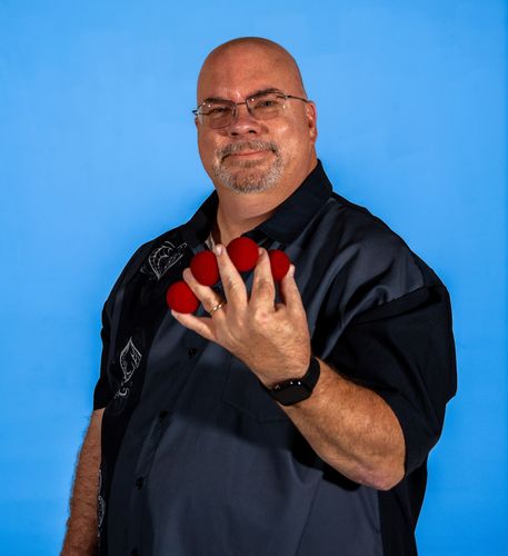 A man in a black and gray shirt is holding 4 red balls in his hand