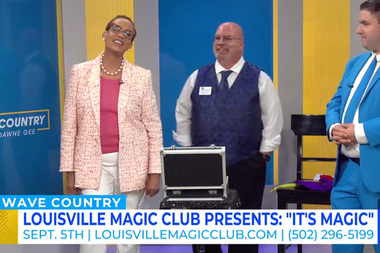 Woman in pink blazer stands beside a magician and another man in a blue suit on a TV set.