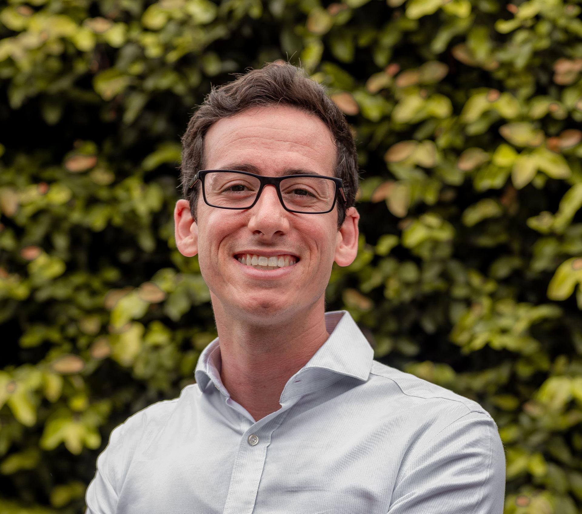 Um homem de óculos e camisa azul está sorrindo para a câmera.