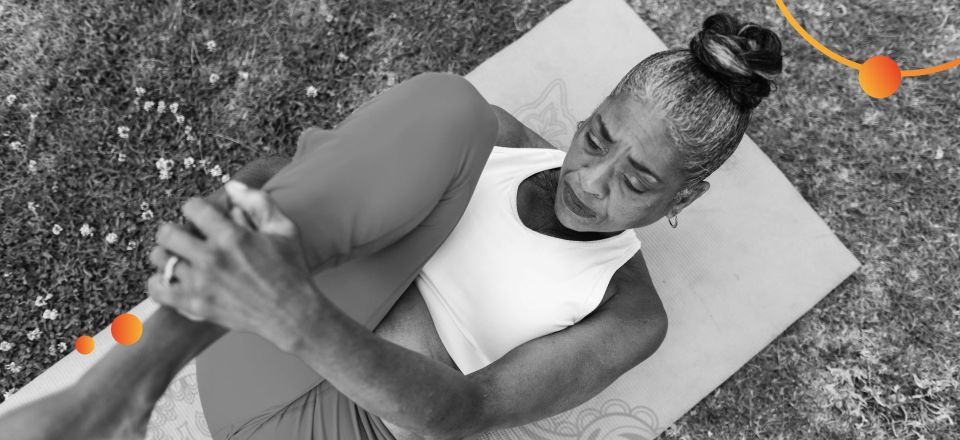Uma mulher negra se alongando em um tapete de yoga no gramado