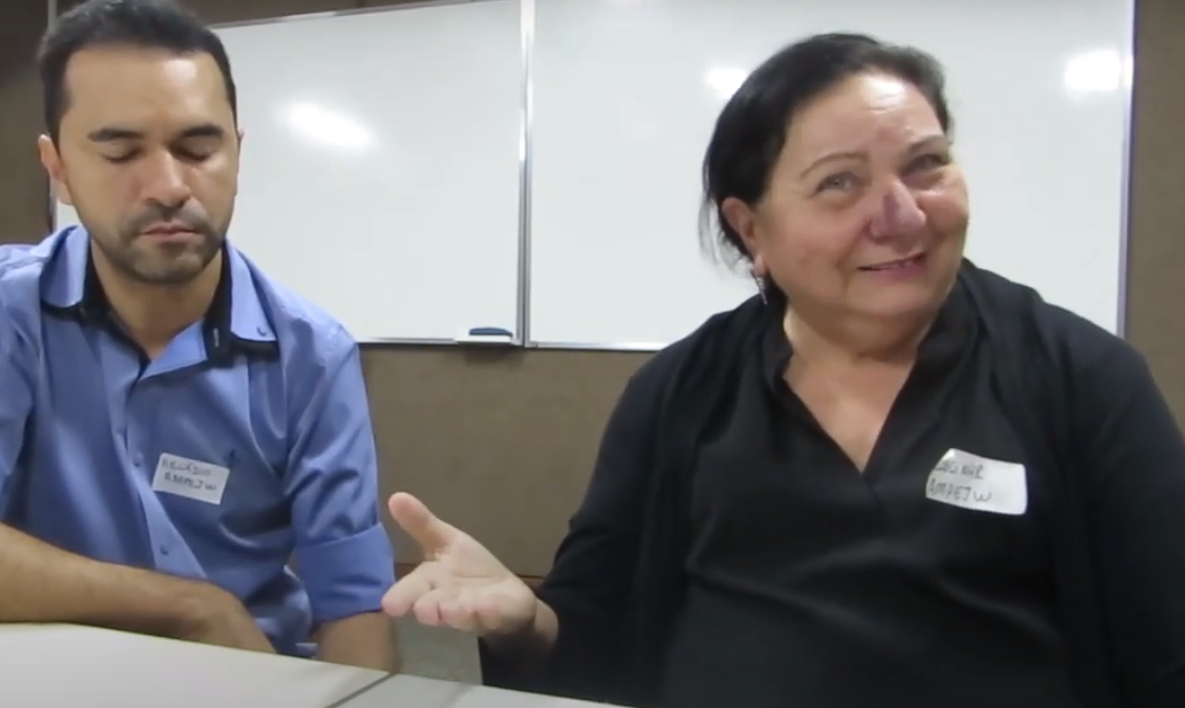 Um homem e uma mulher estão sentados em uma mesa em frente a um quadro branco