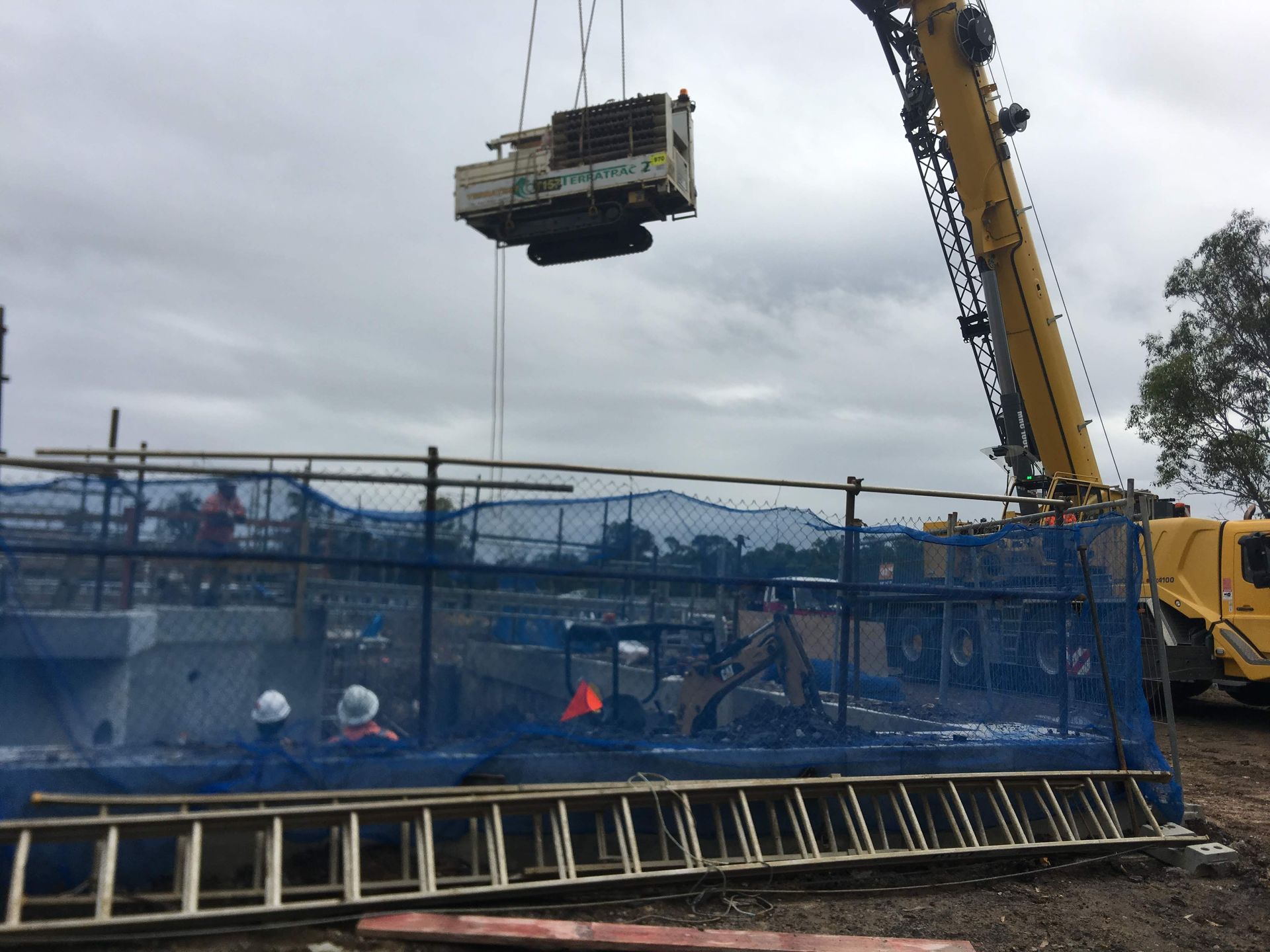 A crane is lifting a machine into the air at a construction site.
