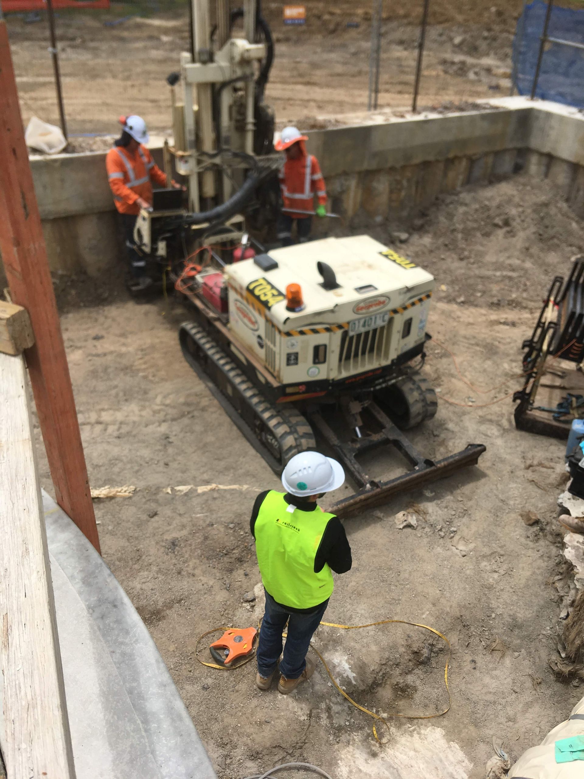 A man in a yellow vest is standing next to a machine on a construction site.
