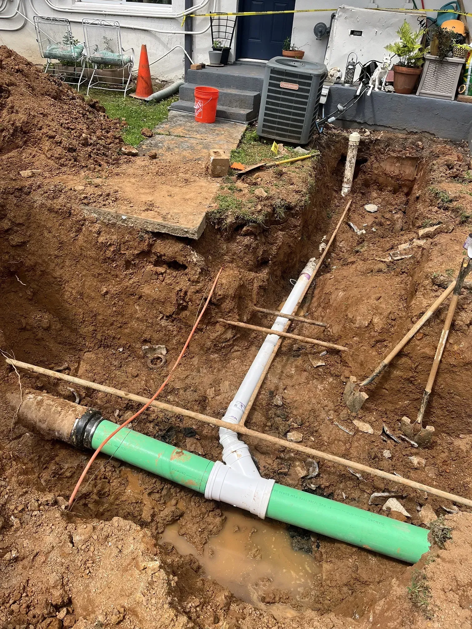 Excavation site with green and white PVC pipes being installed for plumbing near a house.