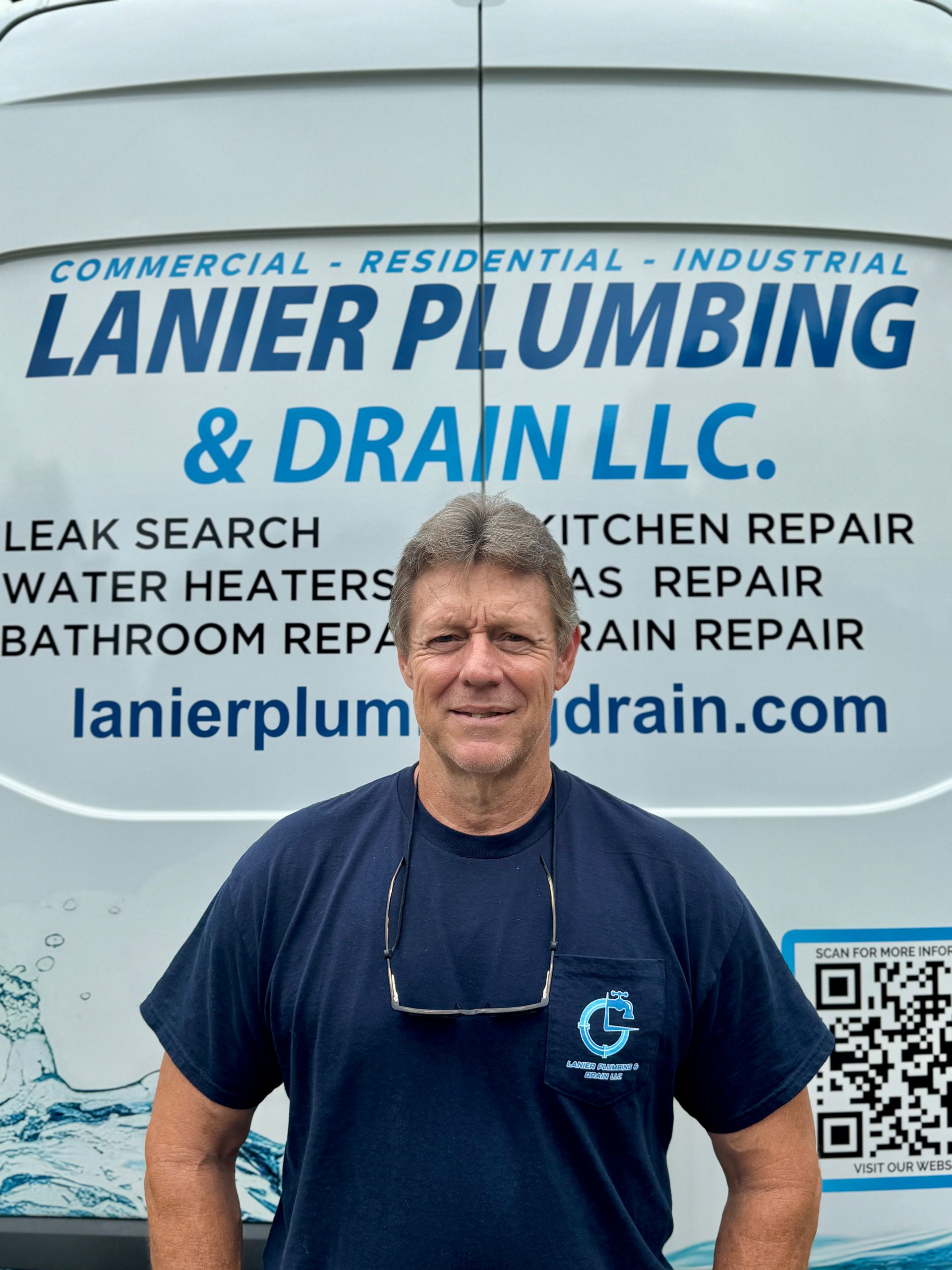 Plumber inspecting under a sink, kneeling with tools in front. He's wearing work clothes and looking intently.