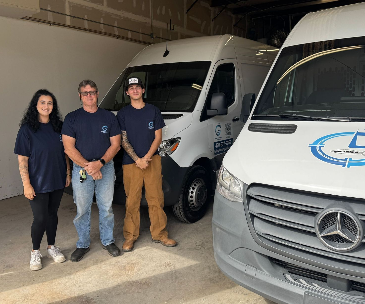 A person wearing overalls works on plumbing in a bathroom. They stand on a toilet with a toolbox in front.