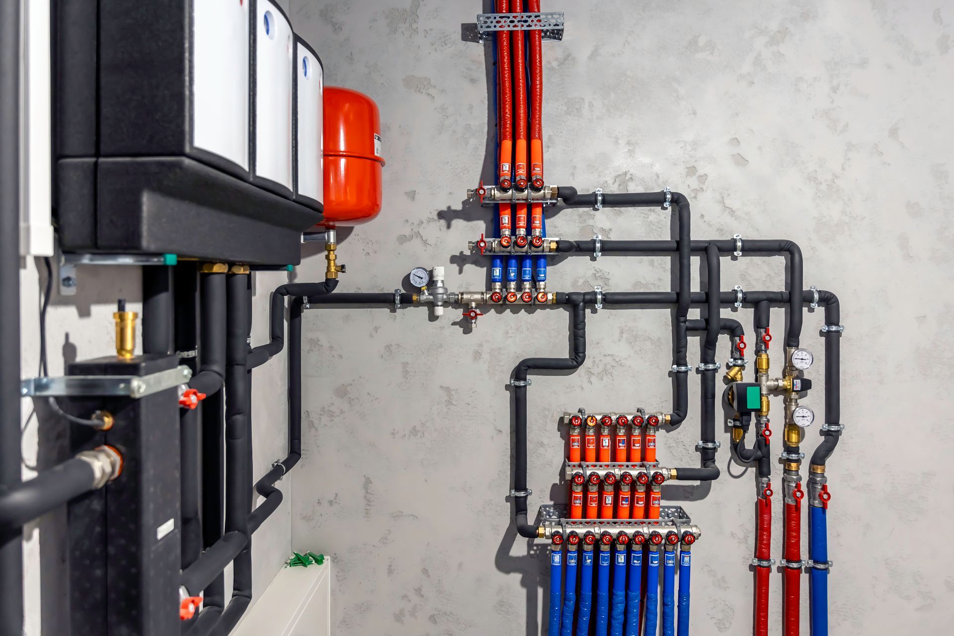 Plumbing system with black, red, and blue pipes connected to heating units on a gray wall.