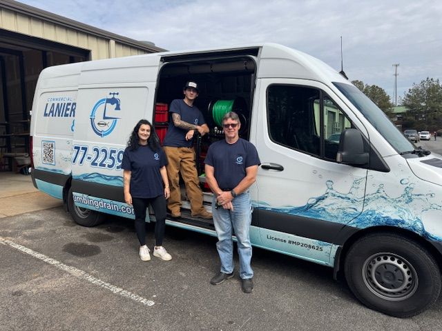 Three staff members stand beside a white plumbing van with blue branding, parked outside an industrial building.