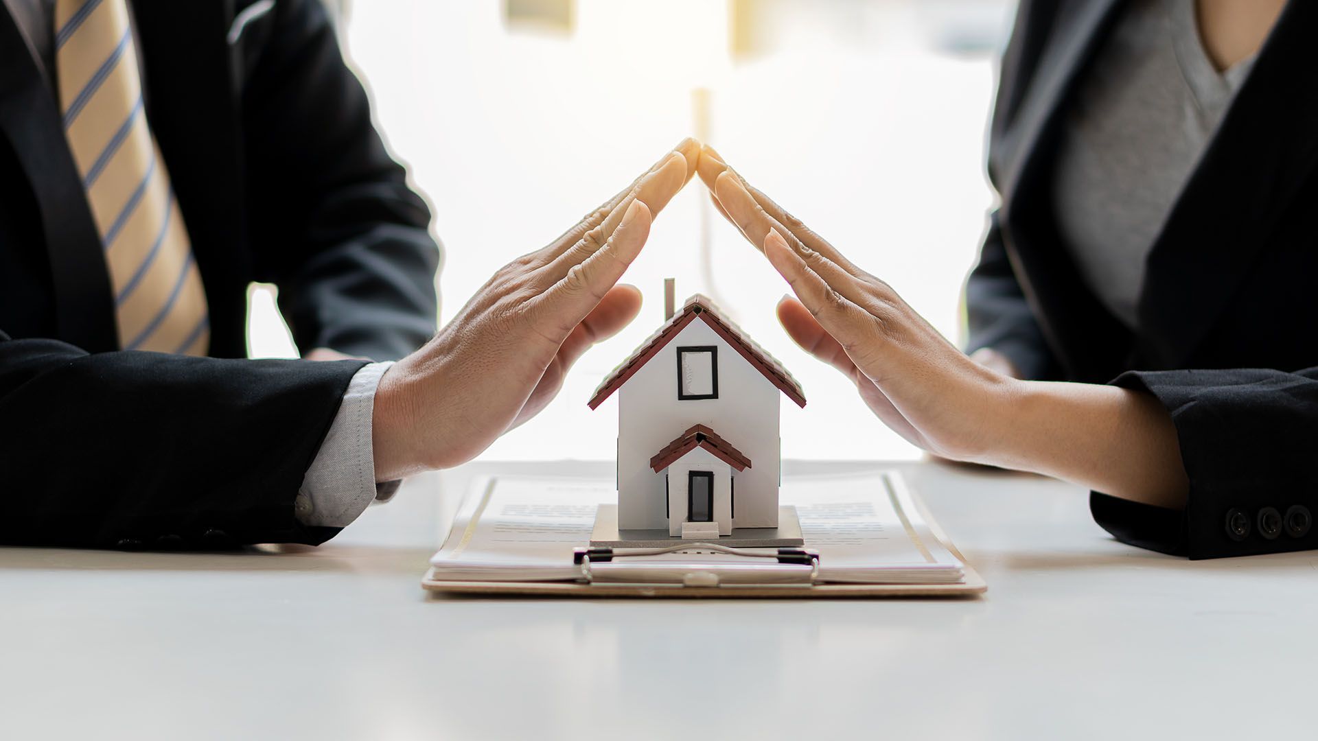 A man and a woman are sitting at a table holding a model house.