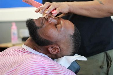 A man is getting his beard shaved by a barber.