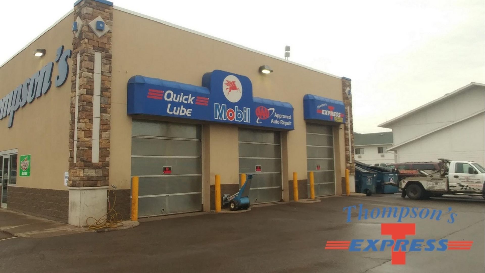 Exterior view of a Thompson’s Express Mobil auto repair and quick lube shop with three service bays under a tan building.